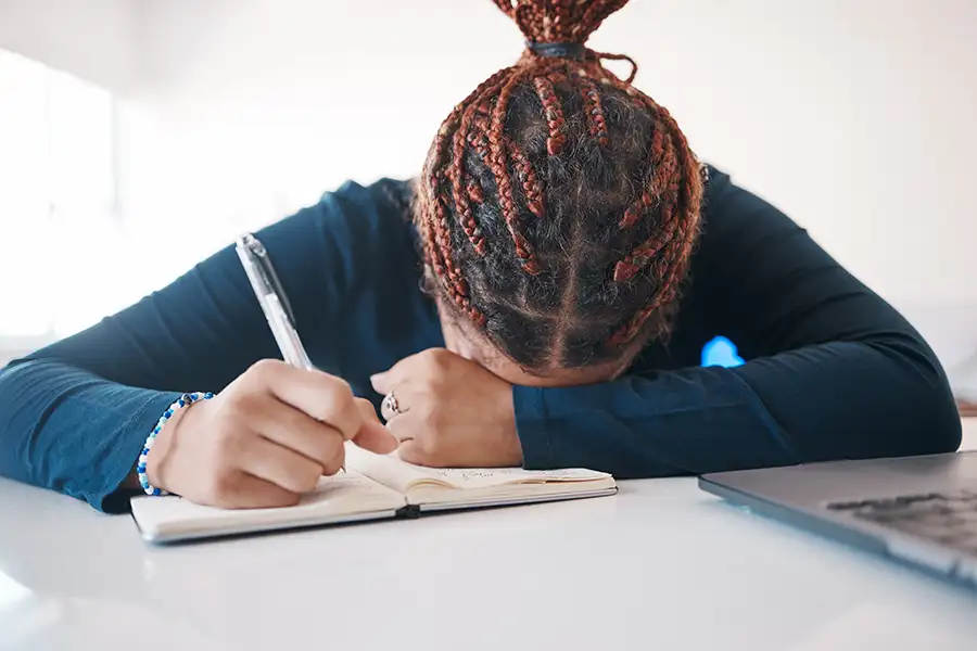 young writer struggling to compose poem, head in arms on desk in frustration - companion image to "Moments" a poem by Shamain Simeon - St. Louis